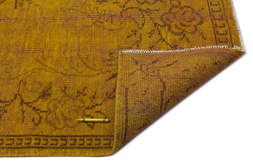 Load image 1 in gallery view. Mustard yellow rug with a faded brown floral pattern and a folded corner, isolated on a white background.