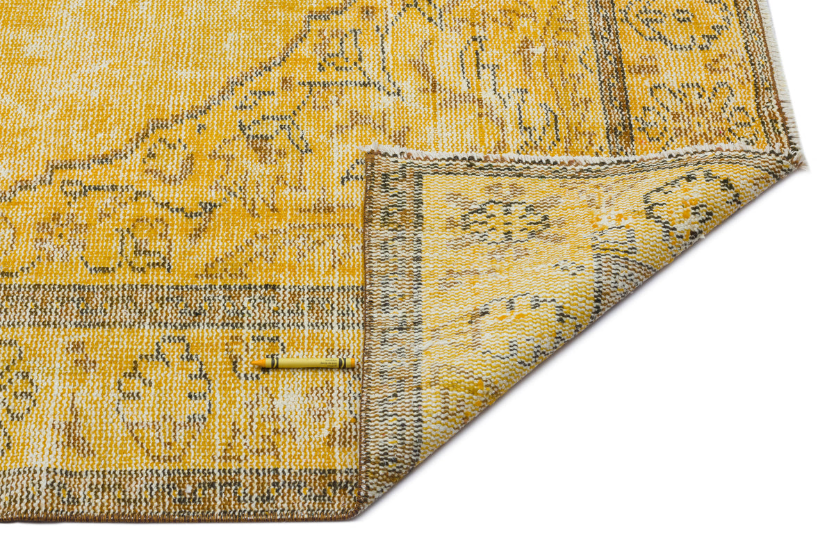 Mustard yellow and white distressed rug with a traditional floral medallion pattern and a folded corner.