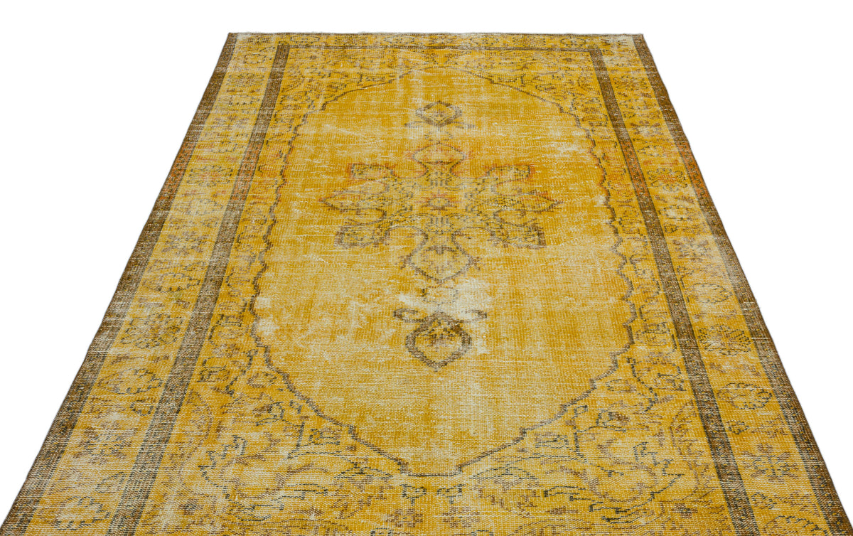 Distressed mustard yellow rug with a faded central floral medallion and brown geometric border on a white background.