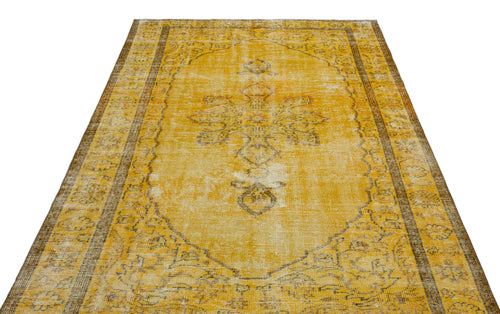 Load image 1 in gallery view. Distressed mustard yellow rug with a faded central floral medallion and brown geometric border on a white background.