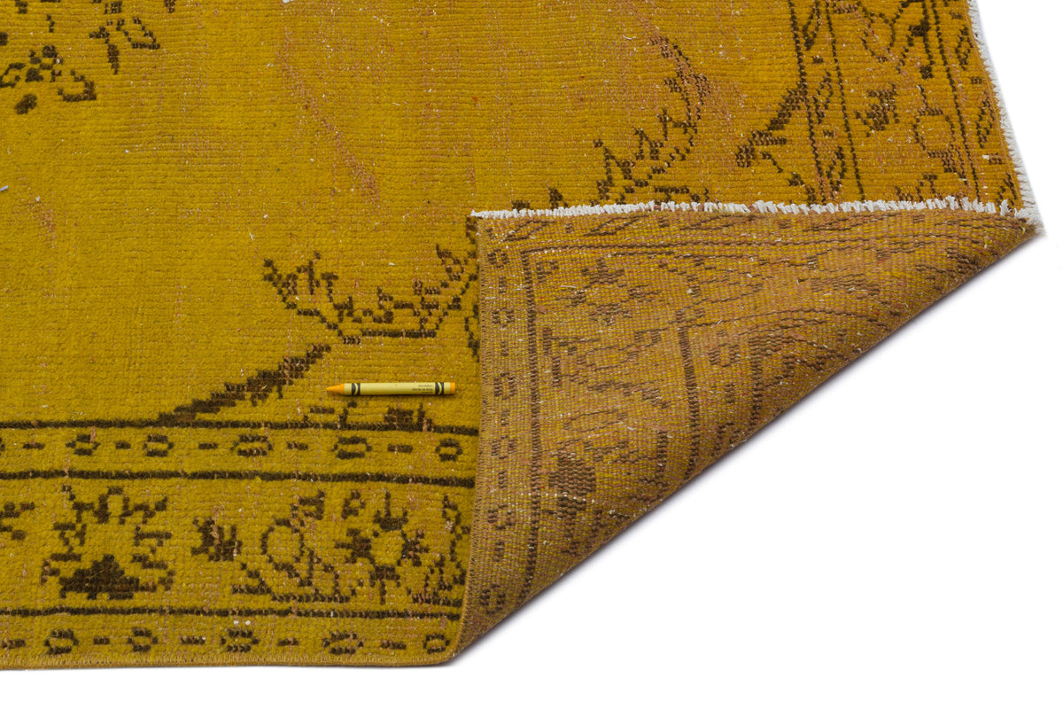 Mustard yellow vintage rug with a dark brown floral border and distressed texture, shown with a corner folded over.