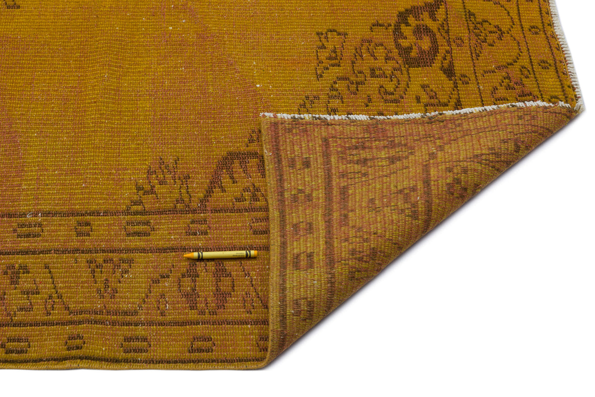 Mustard yellow vintage rug with a faded brown traditional border pattern, shown with a corner folded over.