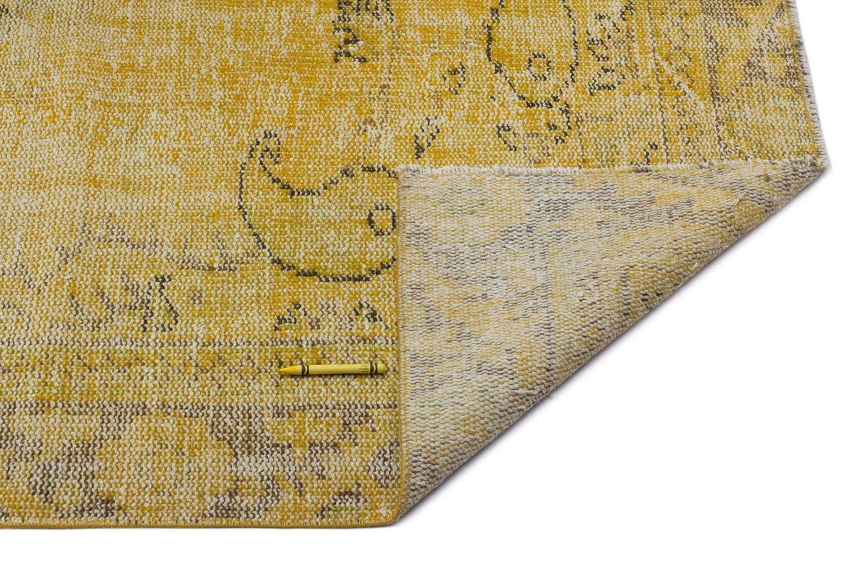 Yellow and beige distressed rug with a faded paisley pattern, shown with a corner folded over on a white background.