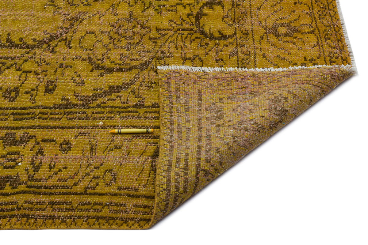 Mustard yellow and brown distressed floral rug with a folded corner and white fringe on a white background.