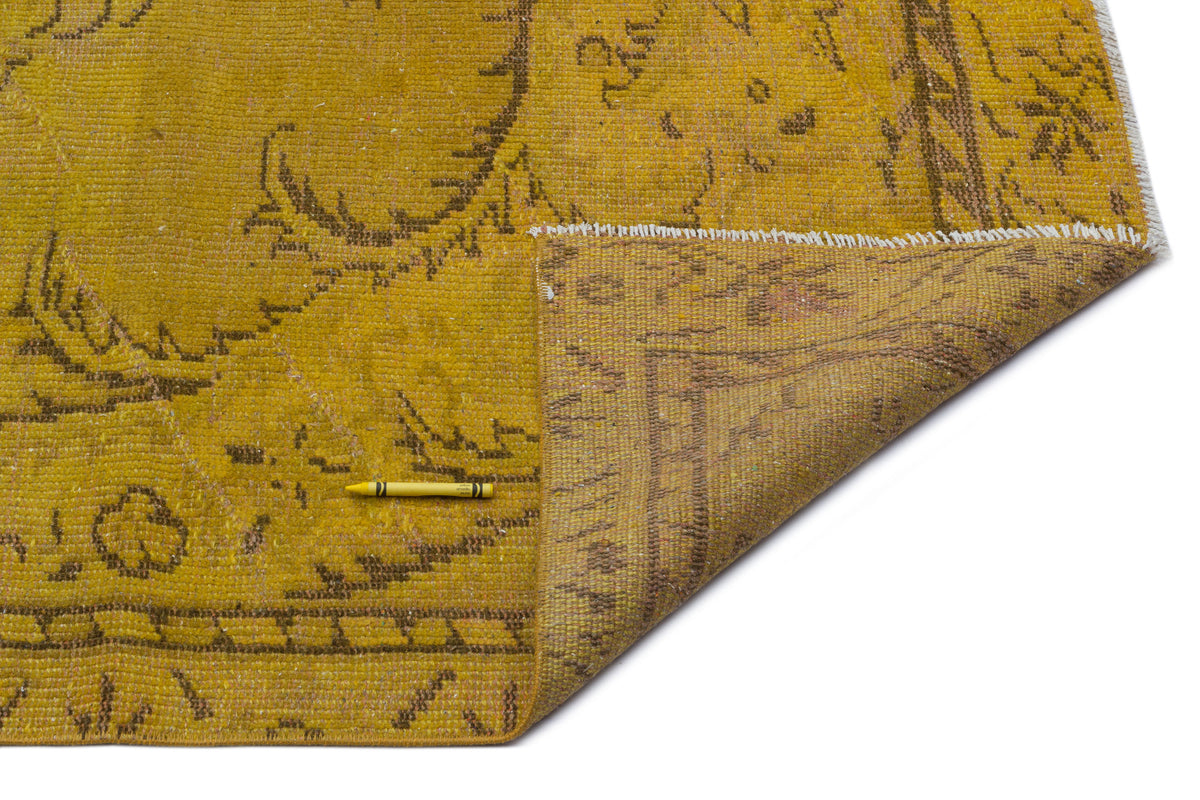 Mustard yellow vintage-style rug with a brown floral medallion pattern, shown with a corner folded over on white.