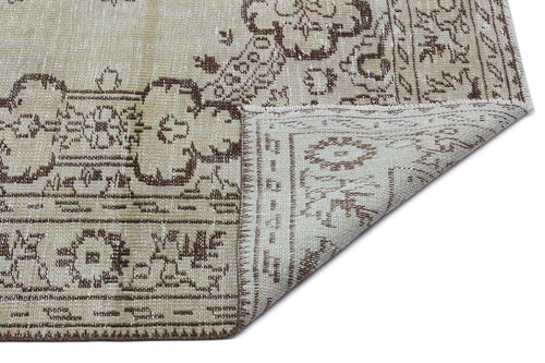Load image 1 in gallery view. Beige and brown vintage-style rug with a distressed floral medallion pattern, shown with a corner folded over.