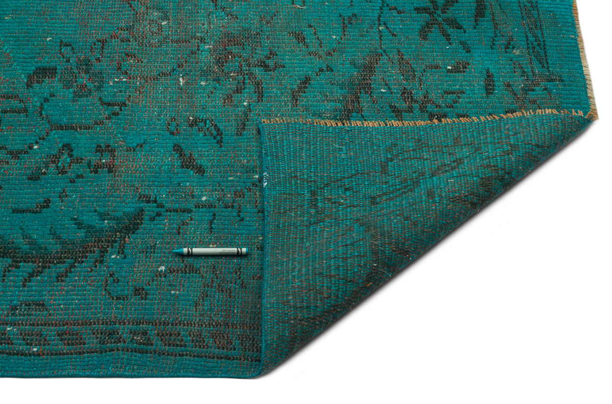 Teal rug with a distressed black floral pattern and a folded corner revealing the woven backing on a white background.