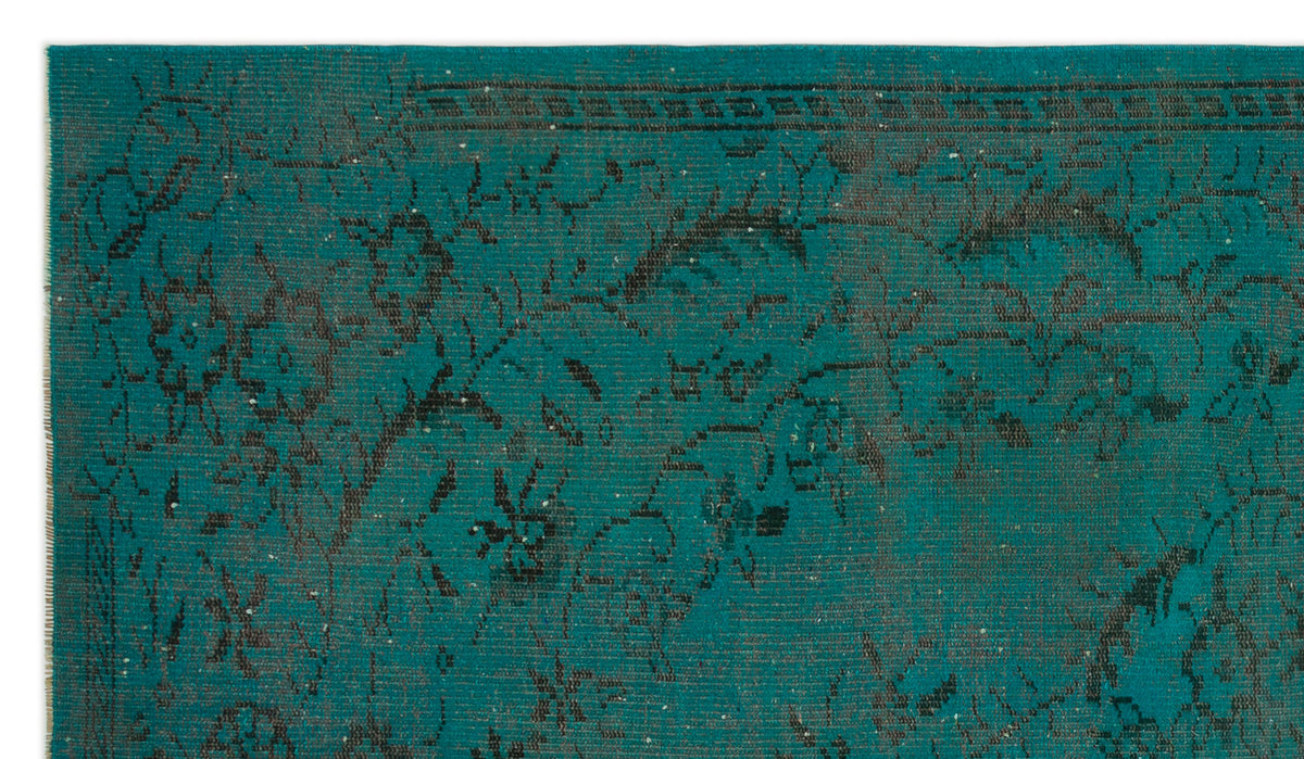 Teal rug with a distressed black floral pattern and a linear border.