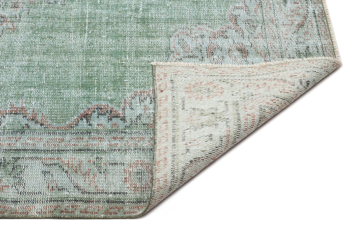 Sage green and terracotta distressed traditional rug with a folded corner revealing the woven backing.