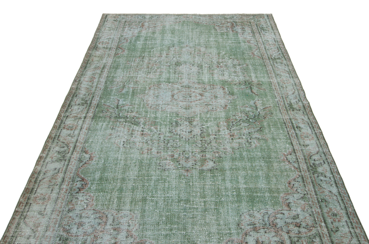 Sage green distressed area rug with a faded central medallion and traditional border pattern on a white background.