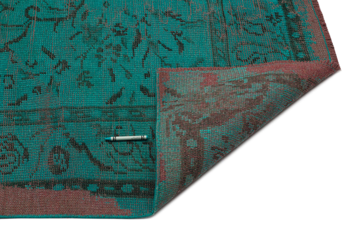 Teal and dark red distressed rug with a traditional floral pattern, shown with a corner folded over on a white background.
