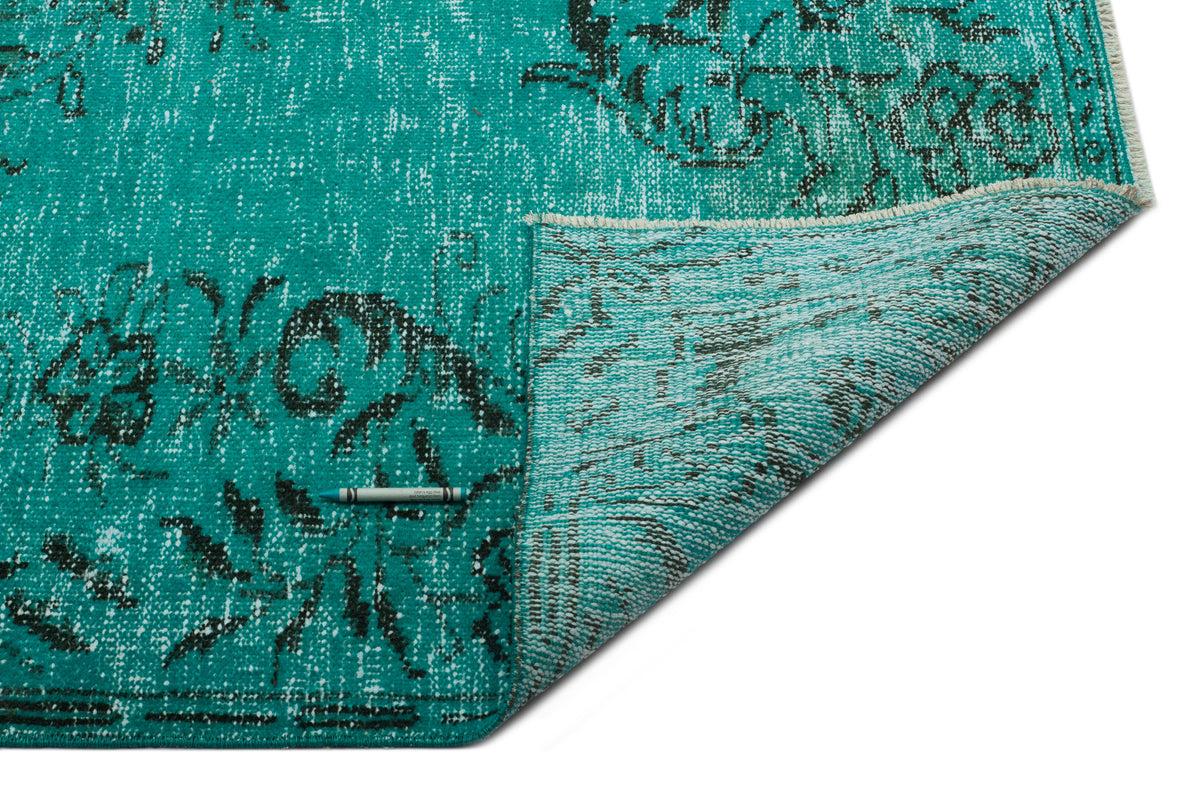 Teal and black distressed floral medallion rug with a folded corner showing the woven backing on a white background.