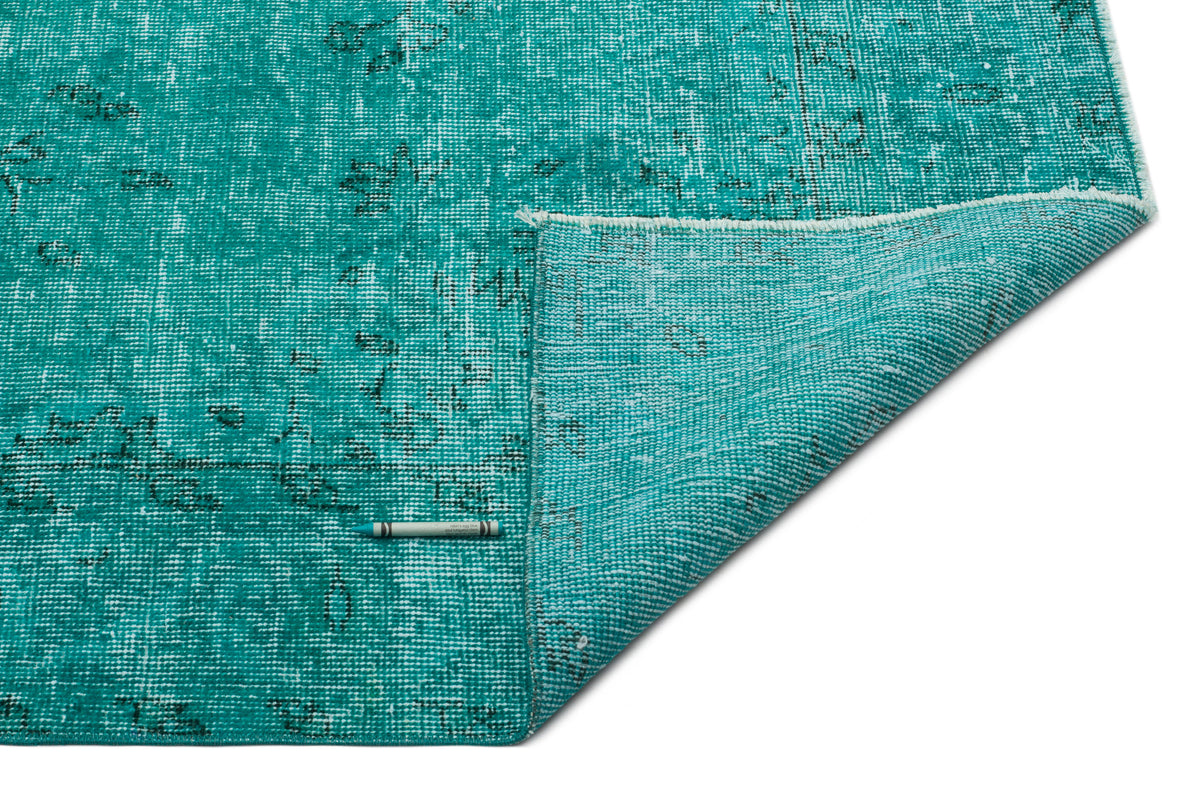 Distressed turquoise rug with a faded black traditional pattern, shown with a corner folded over on a white background.