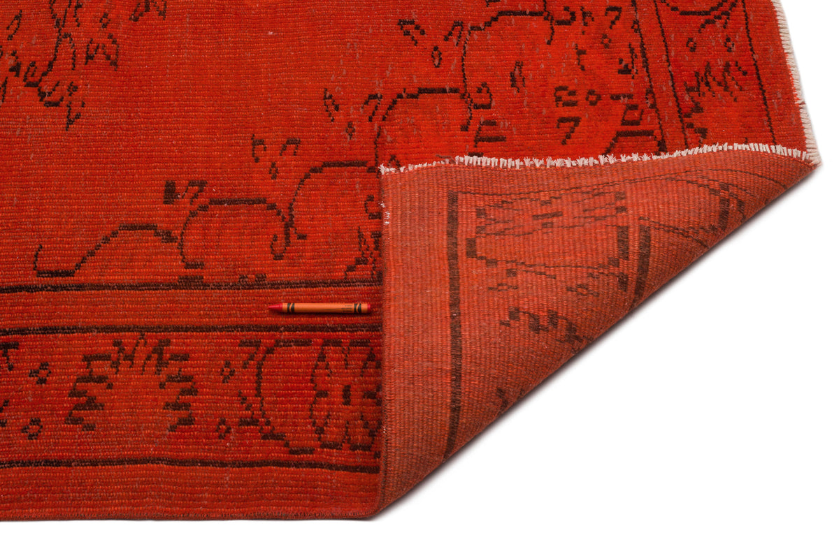 Burnt orange rug with a black geometric border pattern, shown with a corner folded back on a white background.