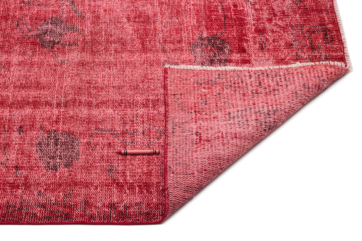 Distressed red rug with a faded floral pattern and a folded corner revealing the woven backing, on a white background.