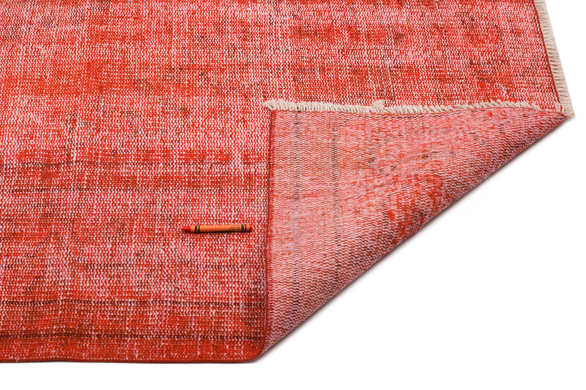 Distressed red and coral overdyed rug with a folded corner, white fringe, and an orange crayon for scale.