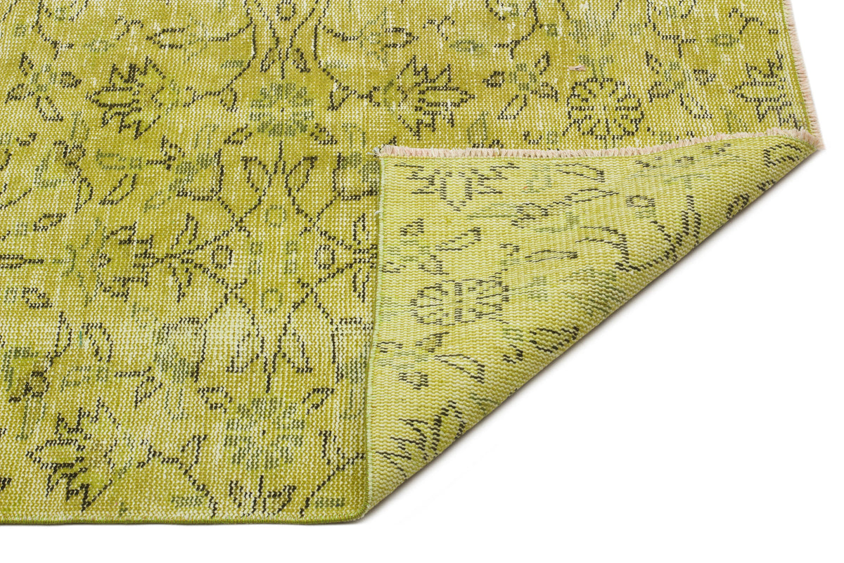 Chartreuse and olive green rug with a distressed floral pattern and a folded corner showing the woven backing.