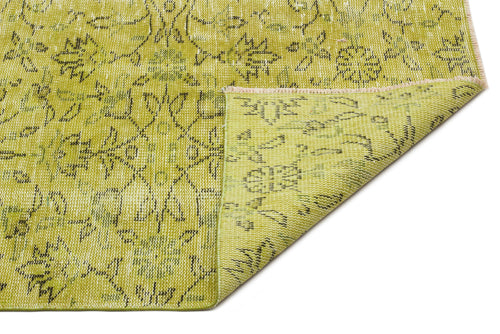 Load image 1 in gallery view. Chartreuse and olive green rug with a distressed floral pattern and a folded corner showing the woven backing.