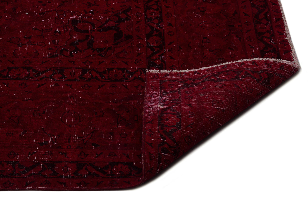 Deep red distressed rug with a black traditional medallion pattern and a folded corner showing the underside.