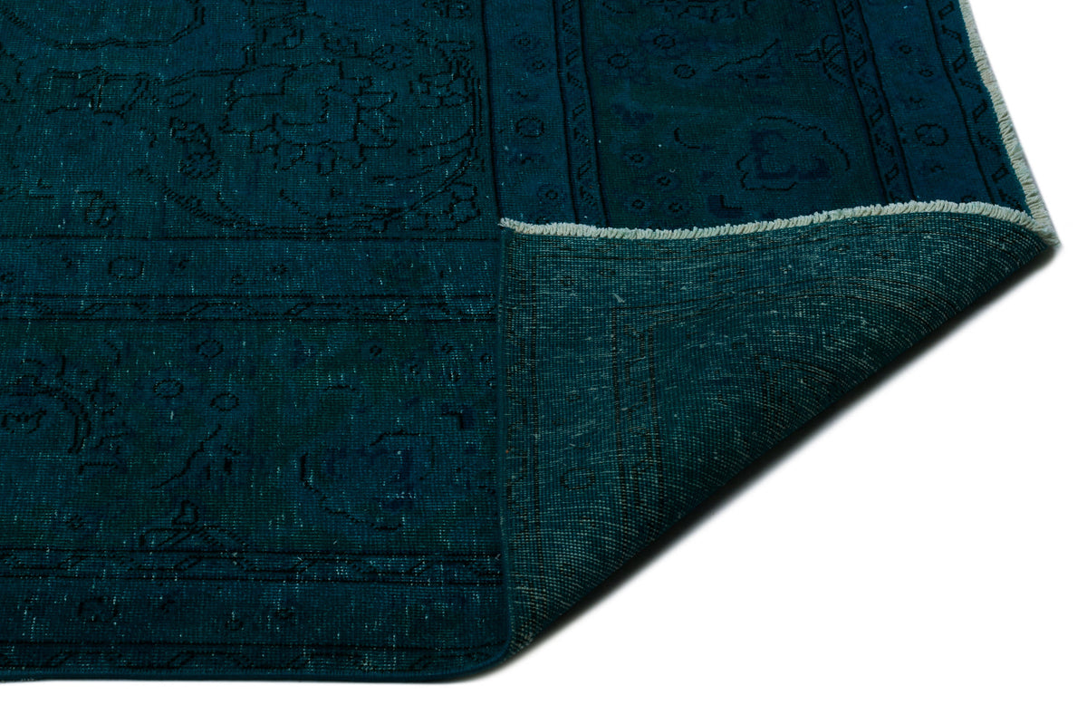 Deep teal traditional rug with a faded medallion pattern and a folded corner showing the woven backing.