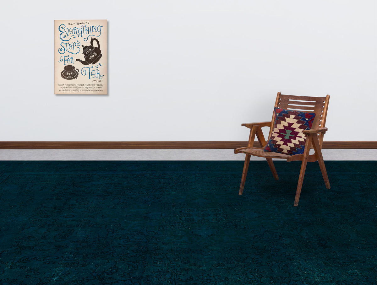 Dark teal rug with a subtle tonal floral pattern, styled in a room with a wooden chair and wall art.