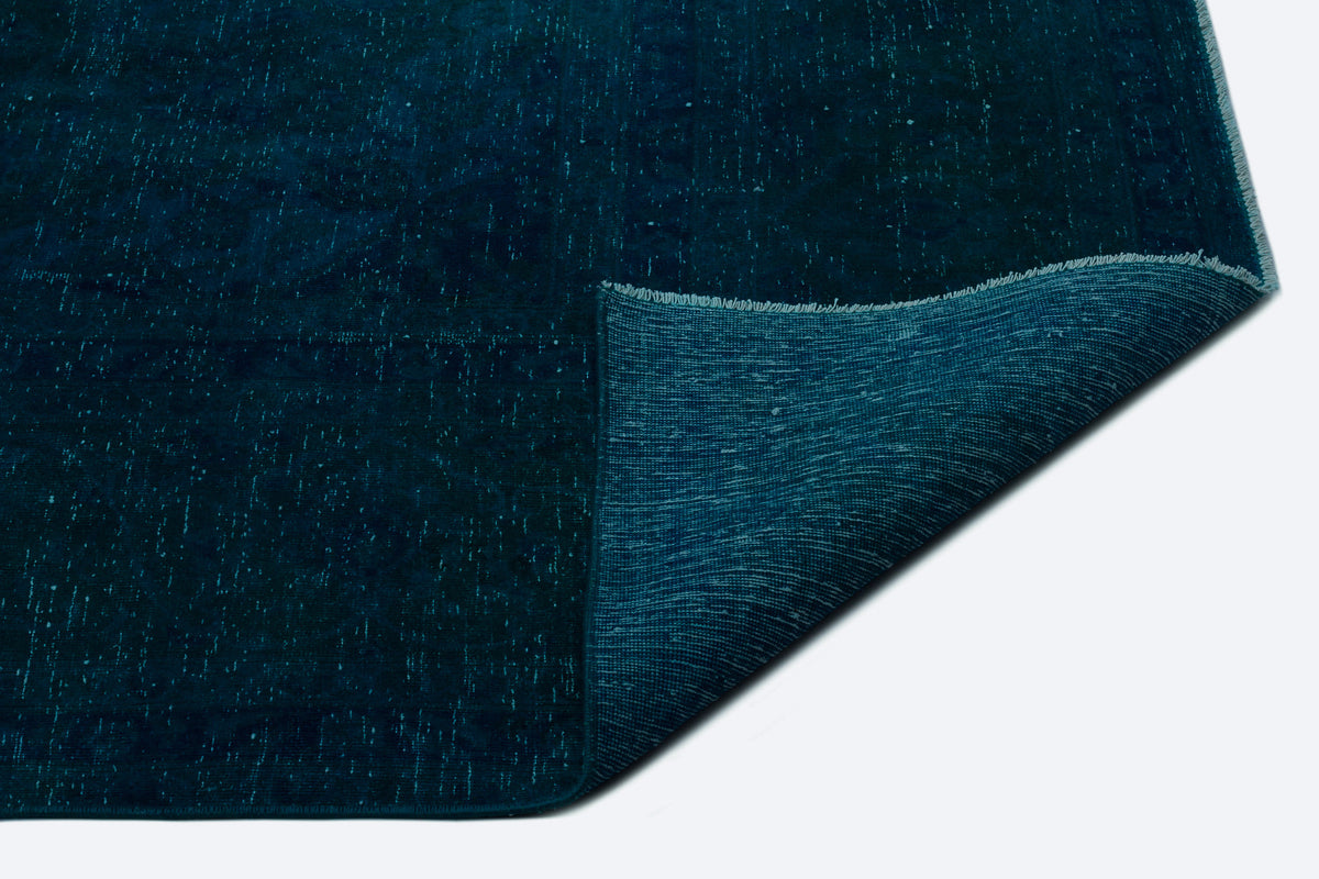 Deep teal rug with a distressed, speckled texture and a folded corner revealing the woven backing.