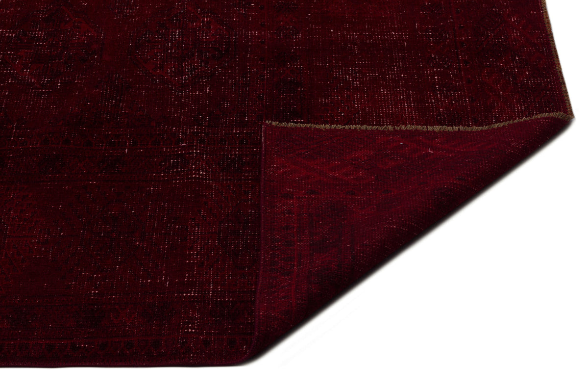 Deep red vintage-style rug with a faint geometric medallion pattern and a folded corner, isolated on white.