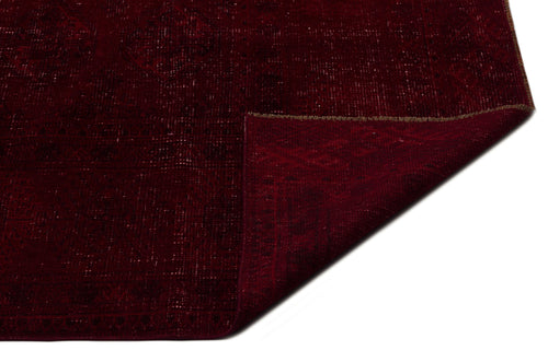 Load image 1 in gallery view. Deep red vintage-style rug with a faint geometric medallion pattern and a folded corner, isolated on white.