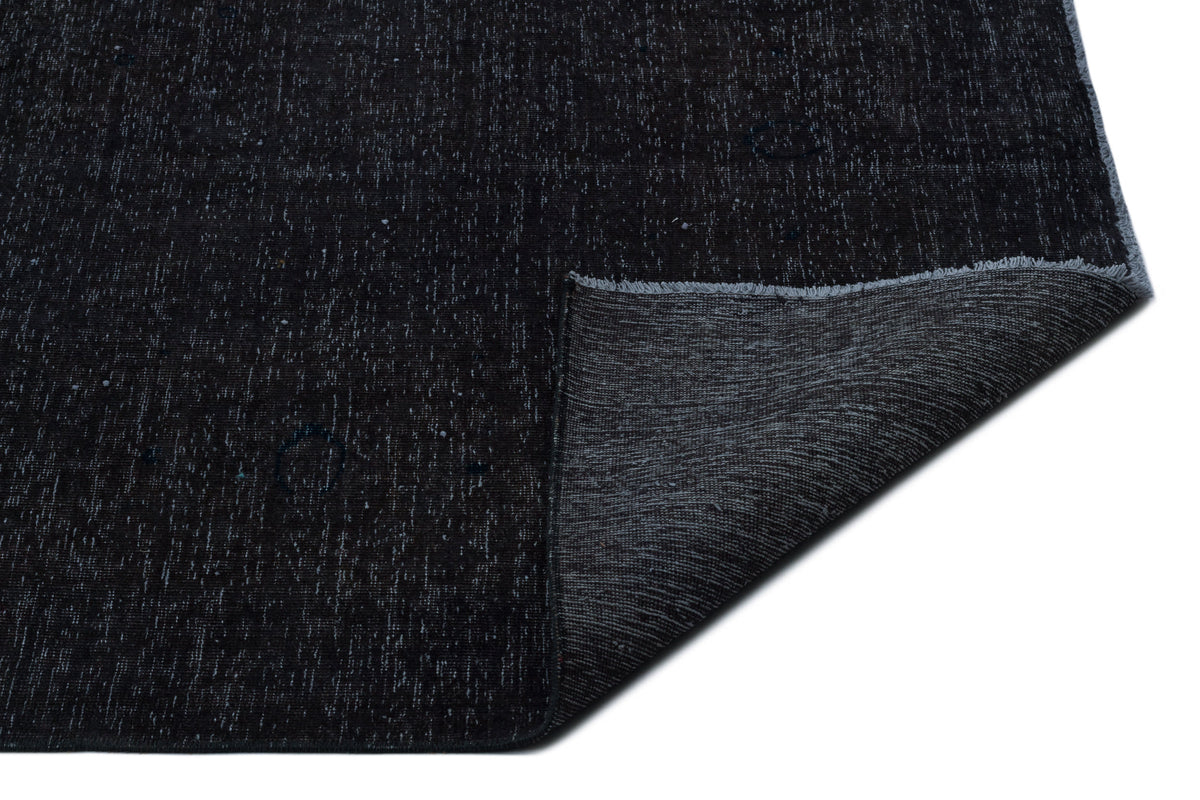 Solid black rug with a subtle white speckled texture and a folded corner revealing a dark grey woven backing.