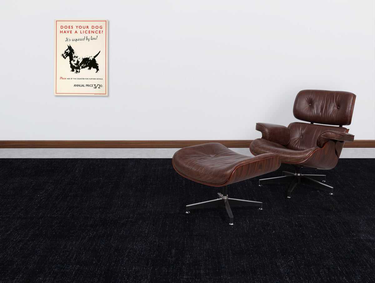 Solid black textured rug in a room with a brown leather lounge chair and vintage dog poster.