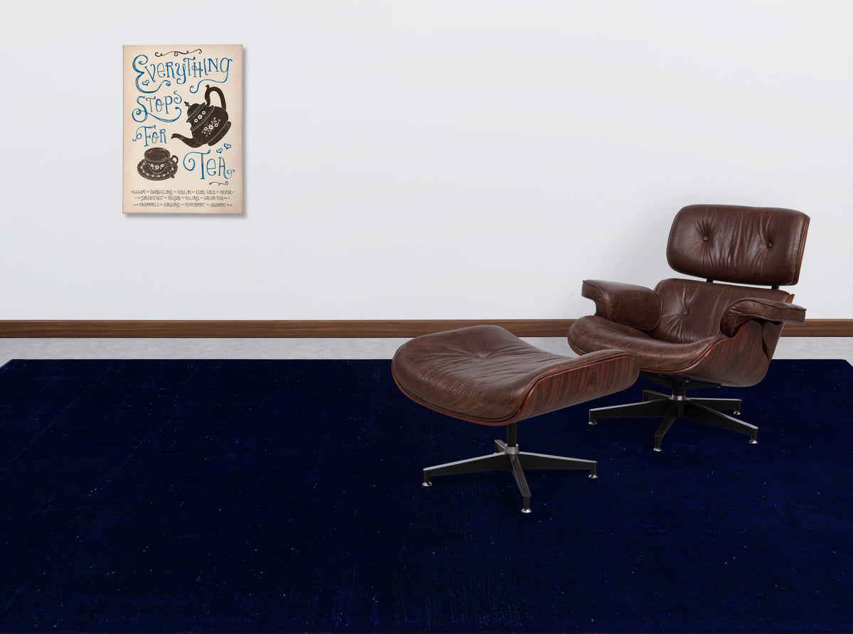 Solid navy blue rug in a room with a brown leather lounge chair and tea-themed wall art.
