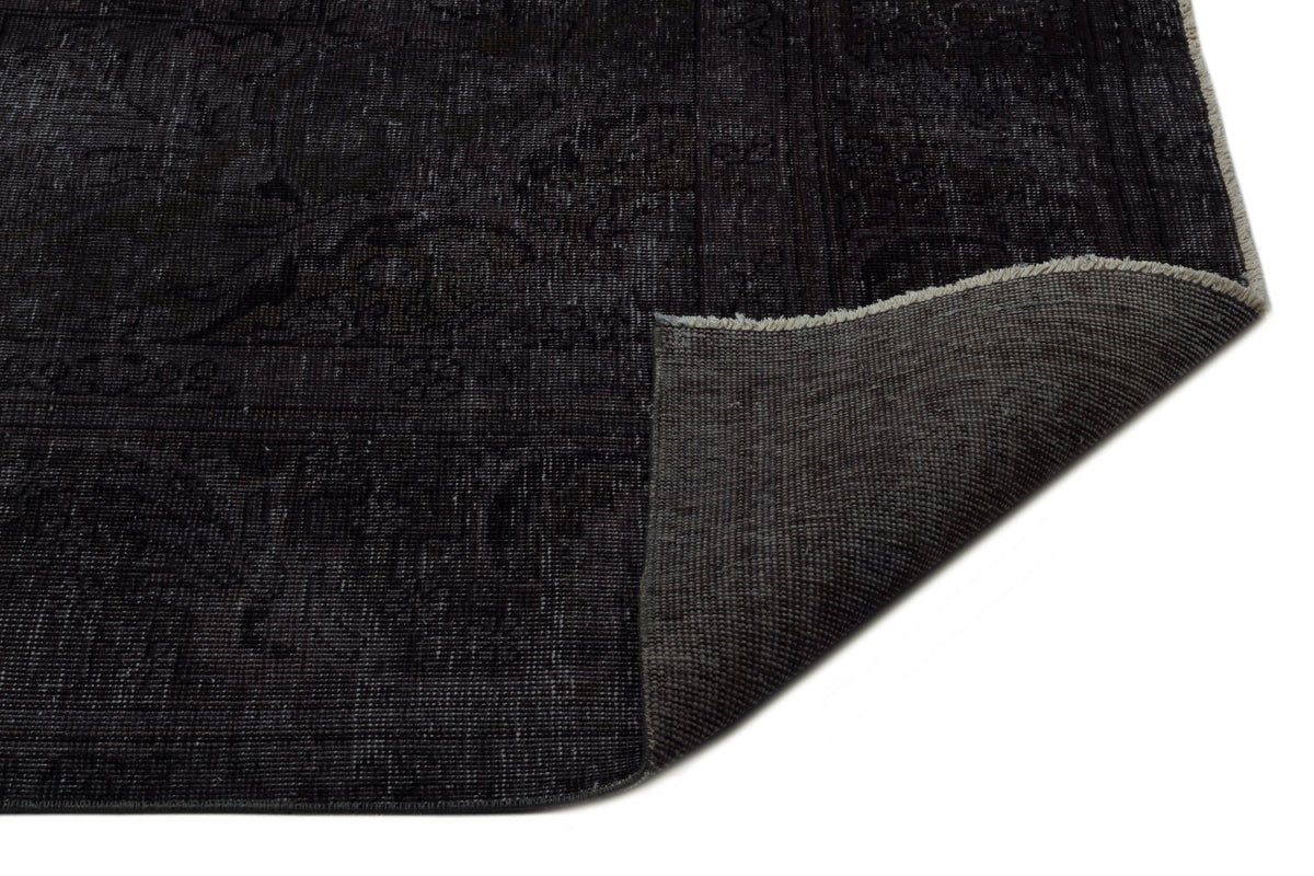 Charcoal black distressed rug with a faint traditional medallion pattern and a corner folded to show the woven backing.