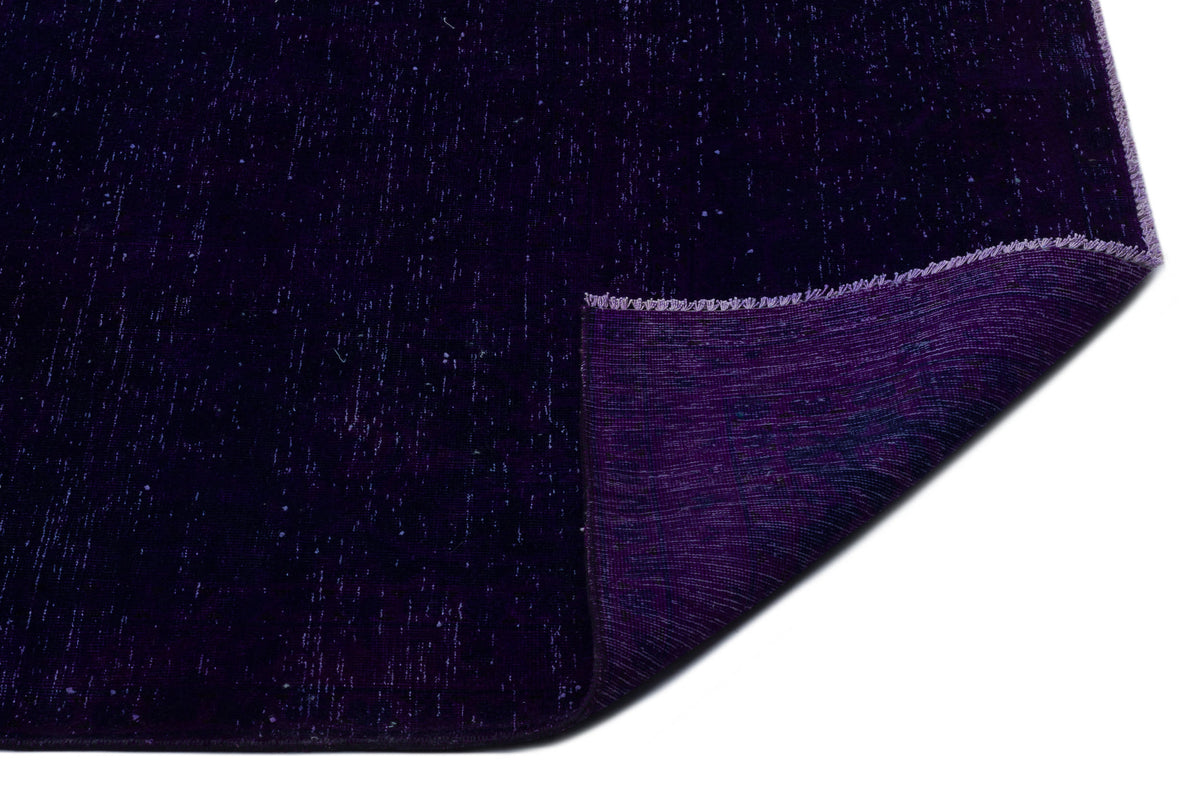 Deep purple rug with a distressed, speckled texture and a folded corner revealing the woven backing.