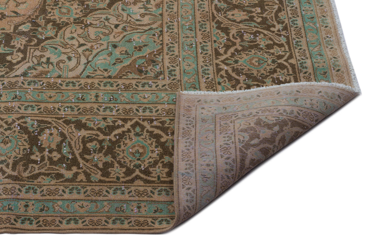 Brown and sage green traditional rug with a distressed floral medallion pattern, shown with a corner folded over.