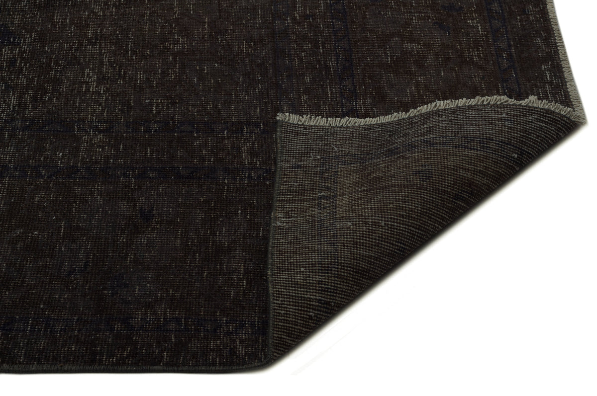 Dark brown distressed rug with a folded corner revealing the woven backing and fringe edge.
