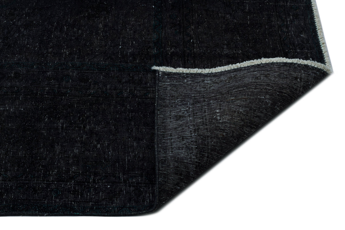 Solid black distressed rug with a folded corner revealing the woven backing and white fringe edge.
