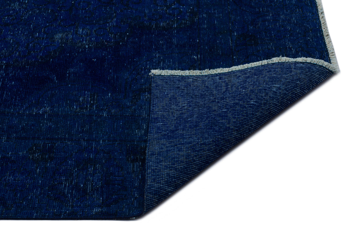 Deep blue distressed rug with a faint traditional pattern and a folded corner showing the woven backing and fringe.