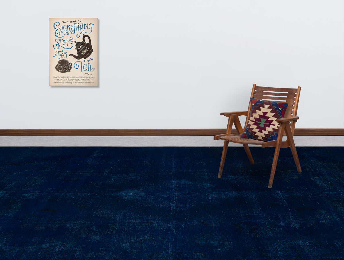Solid navy blue distressed rug in a room with a wooden chair and tea-themed wall art.