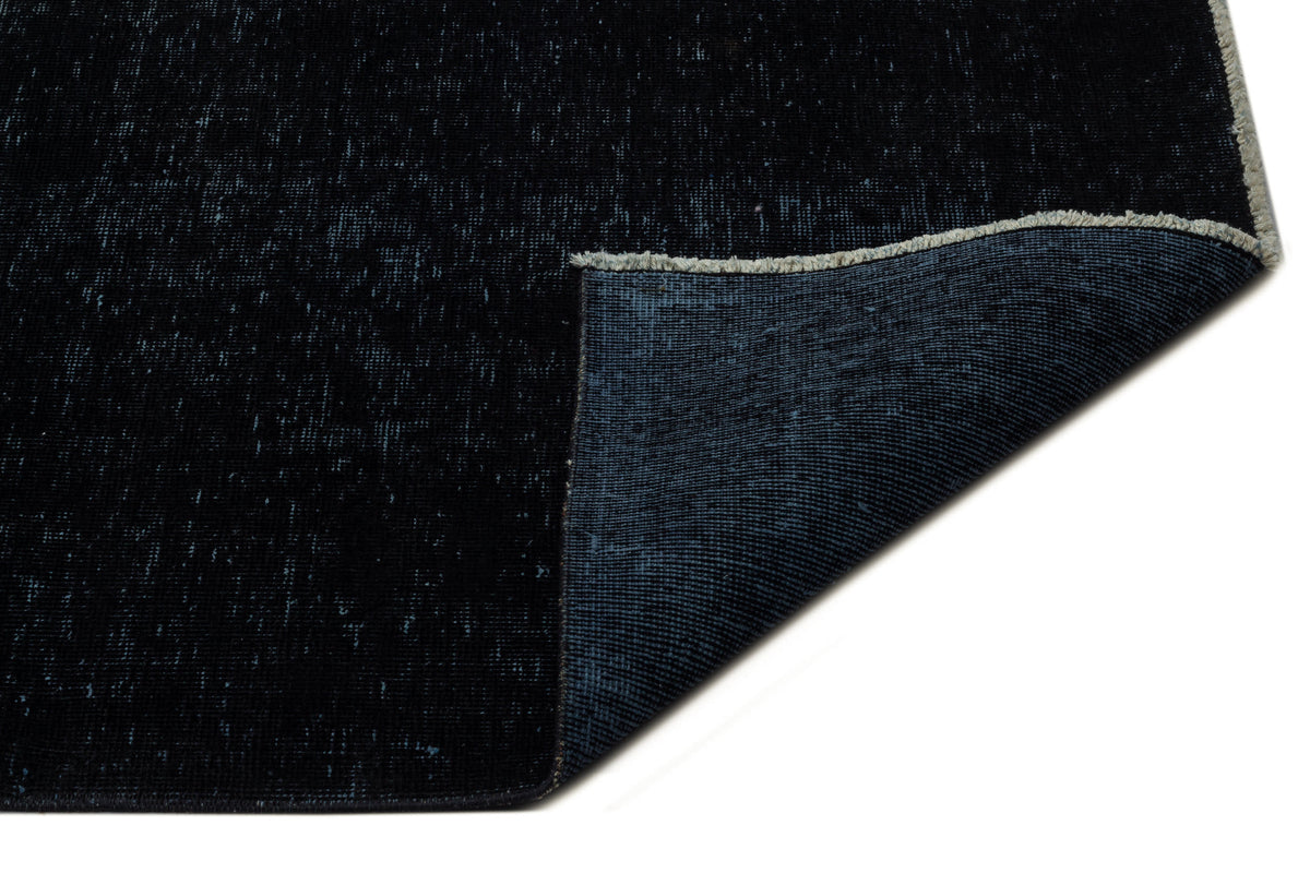 Solid black rug with a distressed texture and a folded corner revealing a dark blue woven backing.