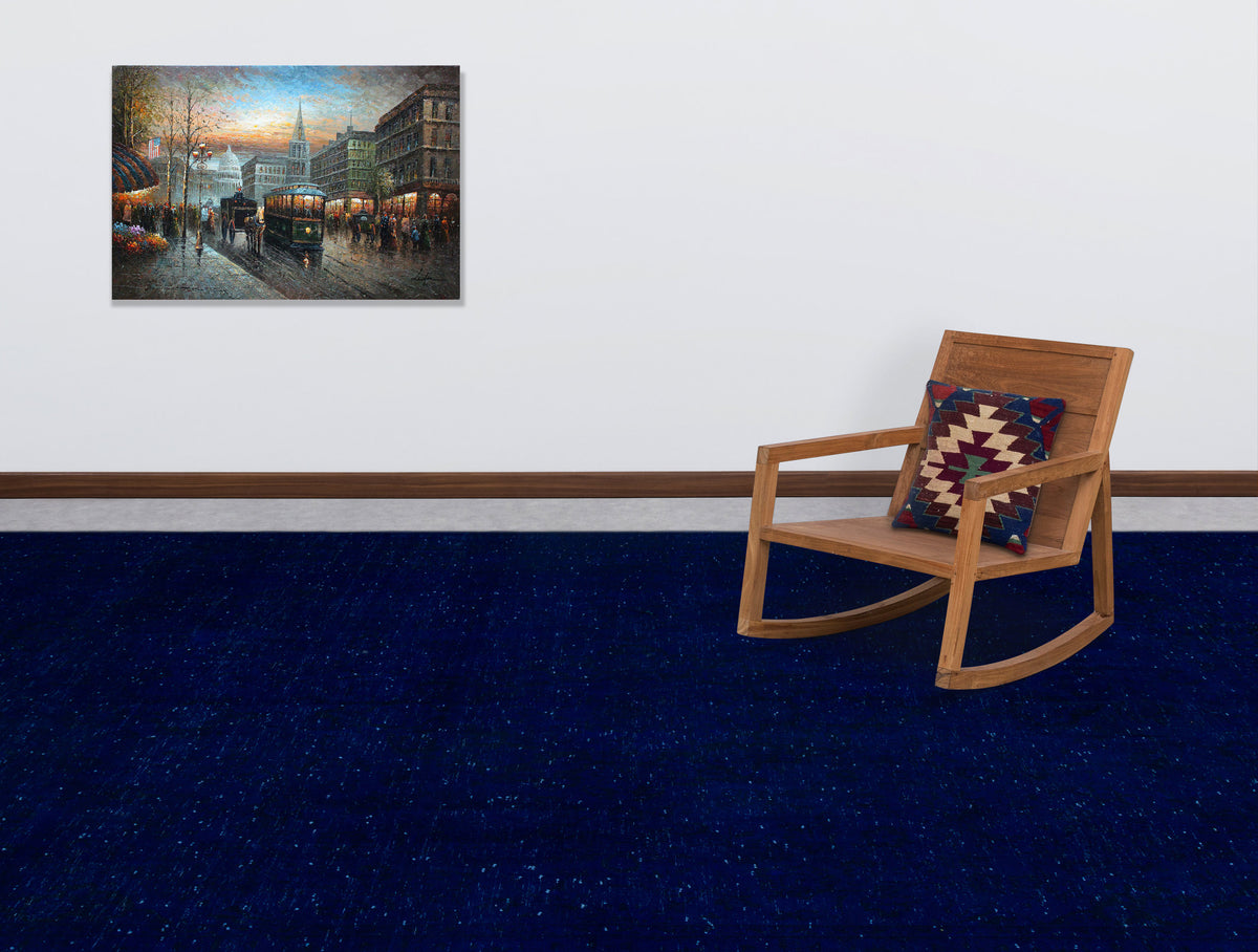 Solid navy blue rug with subtle speckled texture, styled in a room with a wooden rocking chair and wall art.