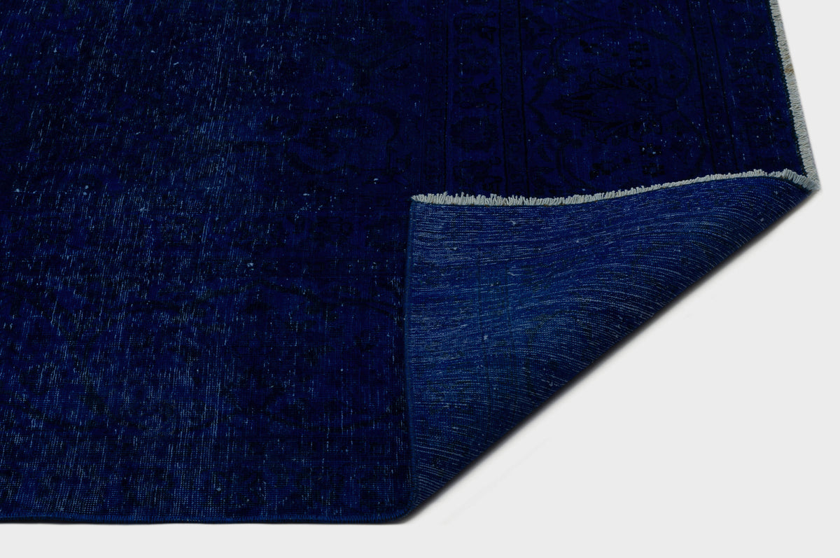 Deep blue distressed rug with a faint traditional medallion pattern and a folded corner revealing the woven backing.
