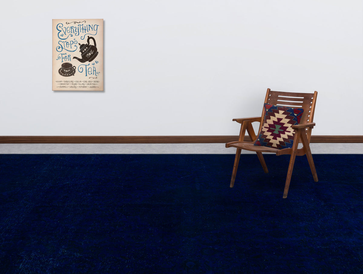 Solid deep blue rug in a room with a wooden chair and wall art.