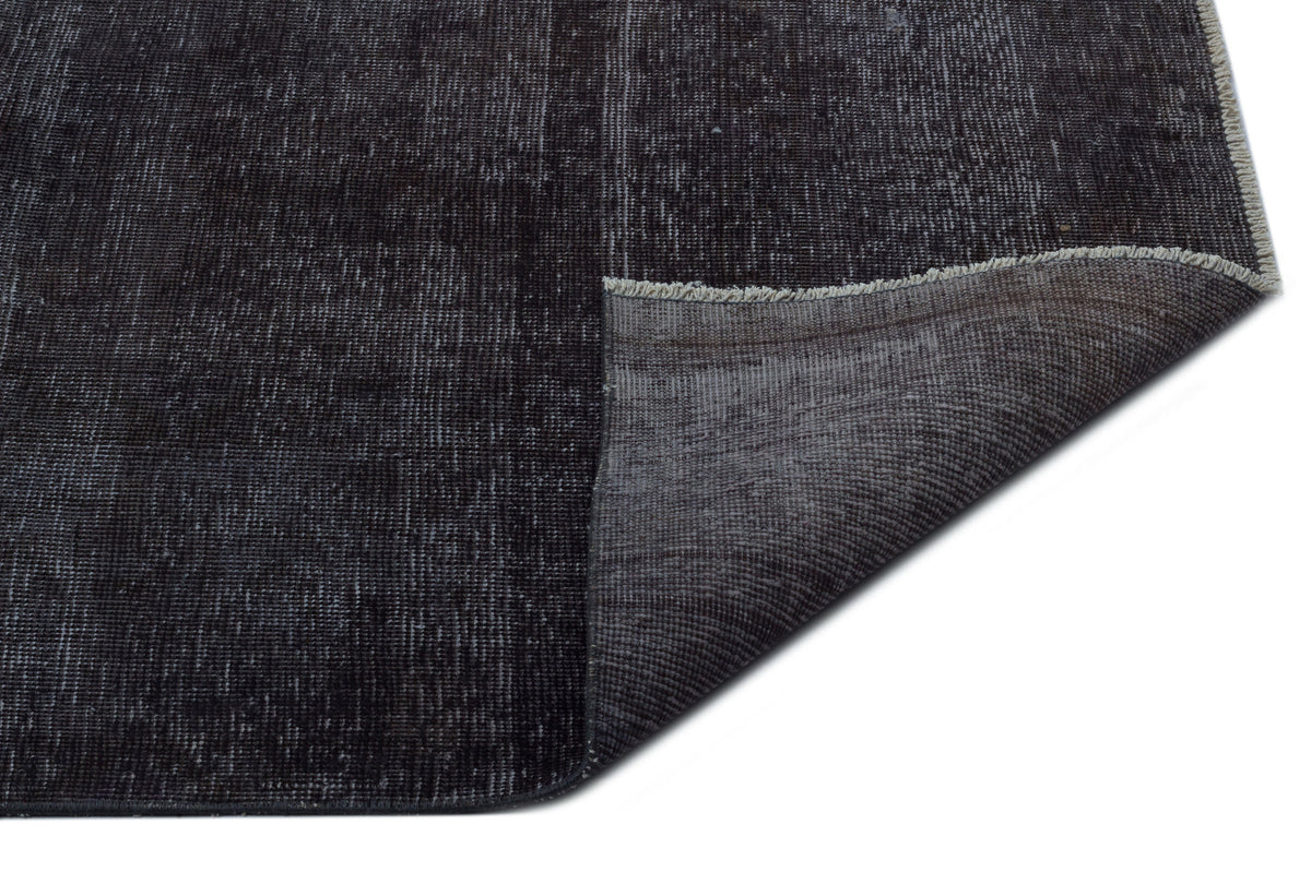 Distressed charcoal and black rug with a folded corner revealing the woven backing and fringe edge.