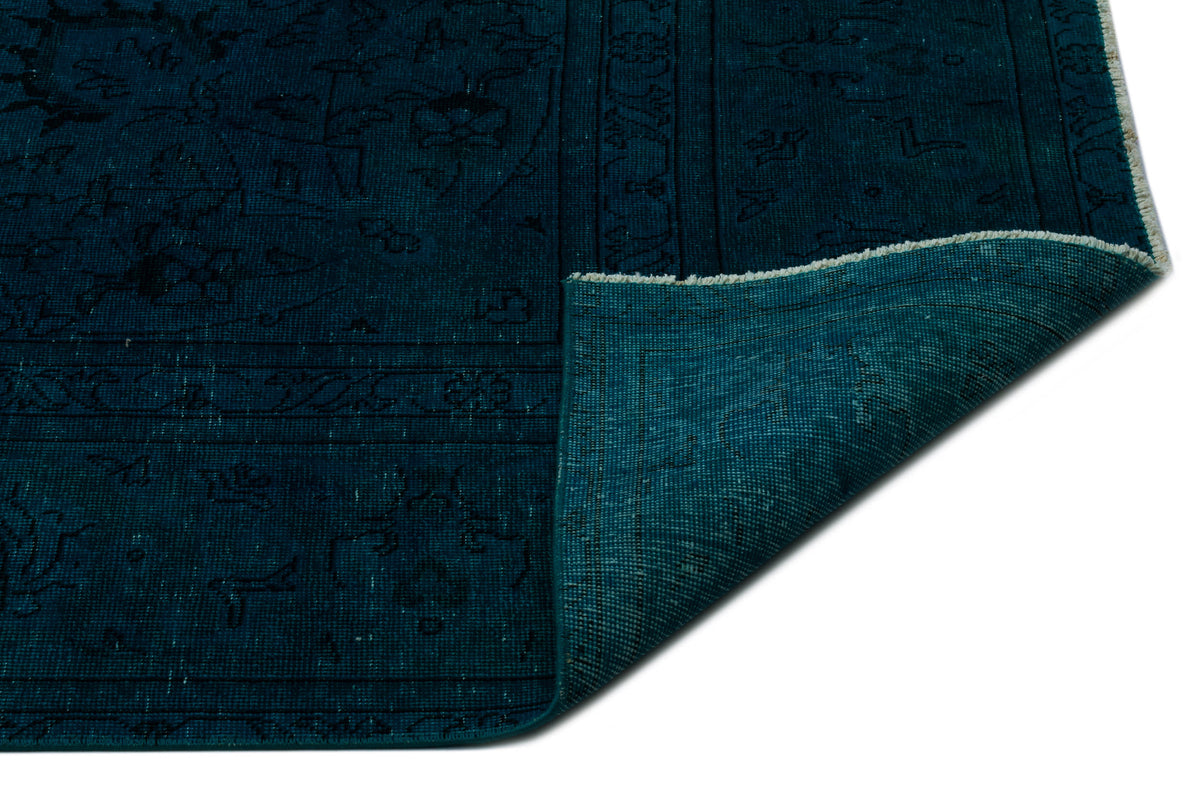 Dark teal rug with a traditional black linear pattern and a folded corner revealing the woven backing.
