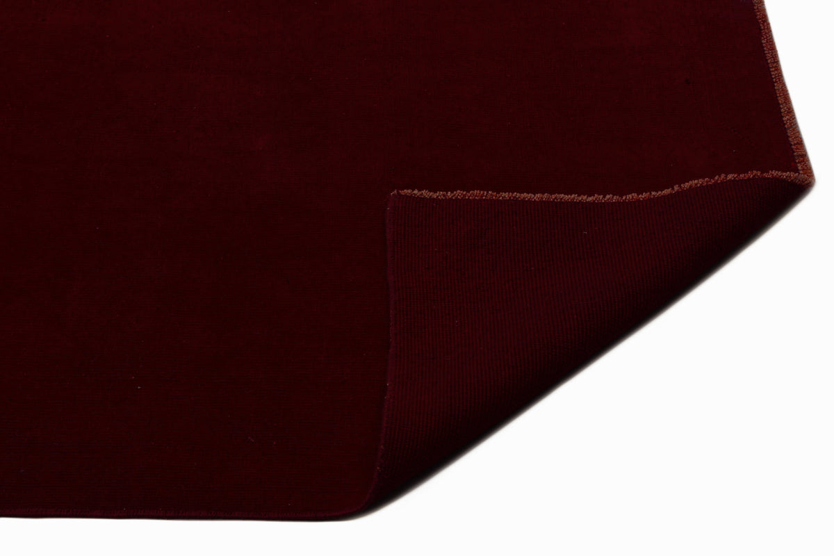 Solid deep burgundy rug with a folded corner revealing the textured underside on a white background.