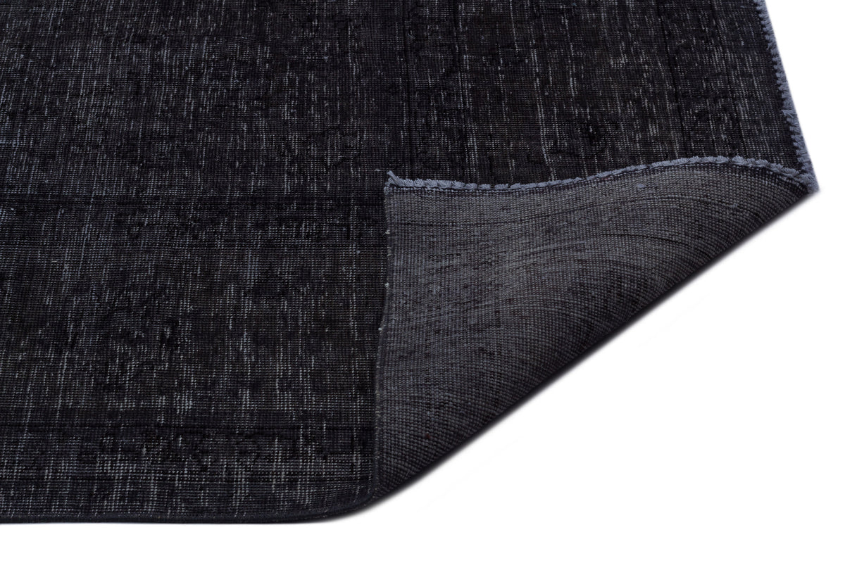 Charcoal black rug with a distressed texture and a folded corner revealing the grey woven backing.