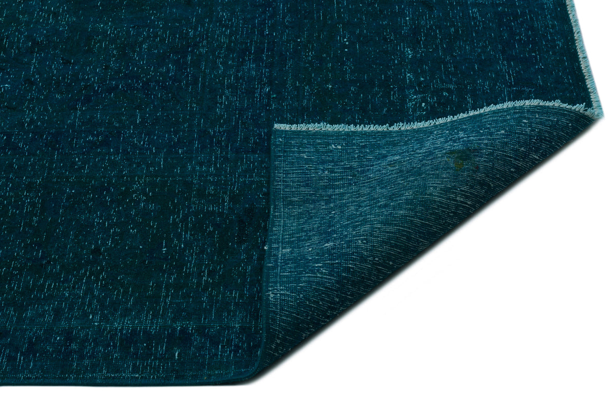 Deep teal distressed rug with a white speckled texture and a folded corner revealing the woven backing.