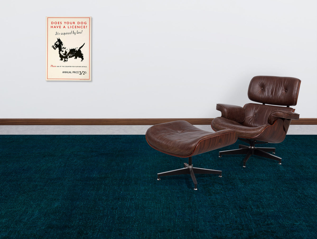 Solid dark teal textured rug in a room with a brown leather lounge chair and a vintage dog license poster.