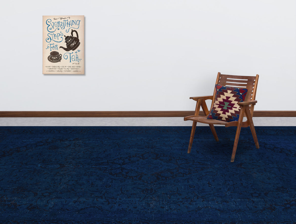 Solid navy blue rug with a subtle tonal floral pattern, styled in a room with a wooden chair and wall art.