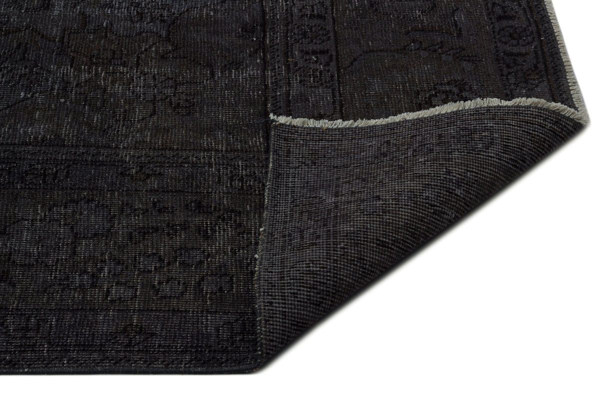 Charcoal black distressed rug with a faint traditional pattern and a folded corner showing the woven backing.